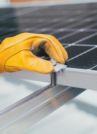 Close-up of a worker's hand with protective gloves adjusting a bolt on a solar panel.
