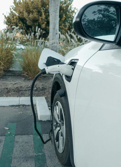 A white electric car plugged into a charger at an outdoor parking area, promoting clean energy.